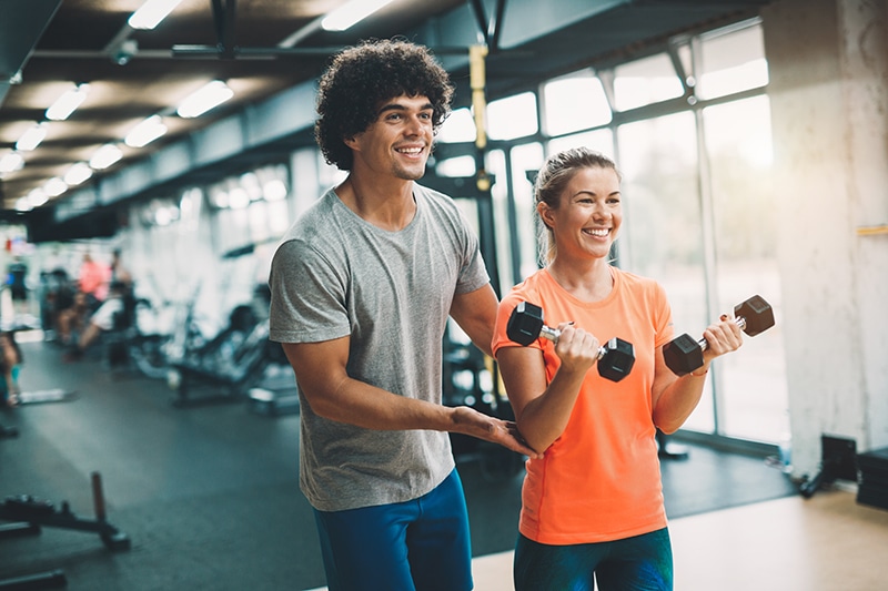 Personal trainer assisting woman lose weight in gym