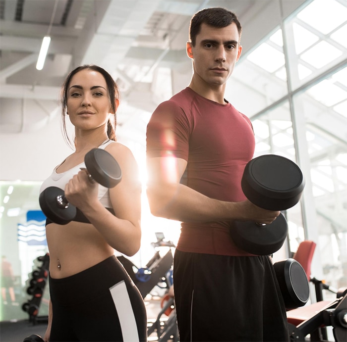 young man and women in a gym lifting dumbbells